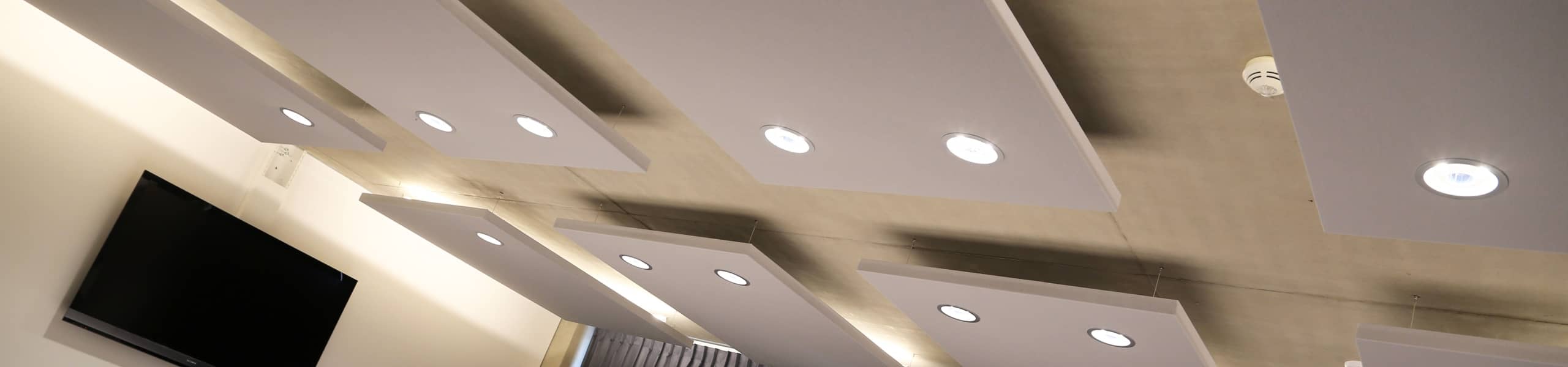 Huit panneaux acoustiques gris avec spots de lumière intégrés sur plafond béton dans salle de réunion professionnelle.