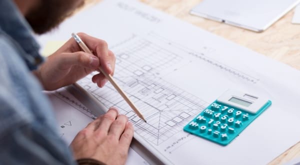 Personne dessinant des plans architecturaux avec une calculatrice à côté