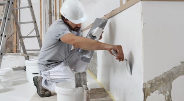 Ouvrier appliquant de l’enduit sur un mur avec une spatule.