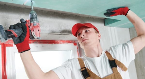 Plaquiste installant des plaques de plâtre au plafond avec une visseuse.